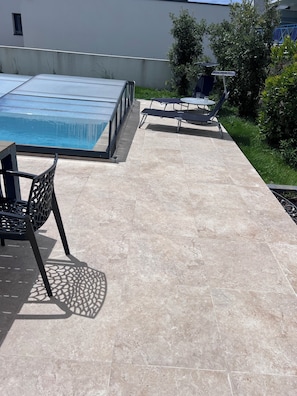 A rooftop pool area with a chair, a table, and a small table with chairs.