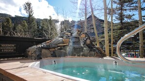 Ein Pool mit einem Wasserfall-Element aus Stein, umgeben von Bäumen und mit Bergblick.