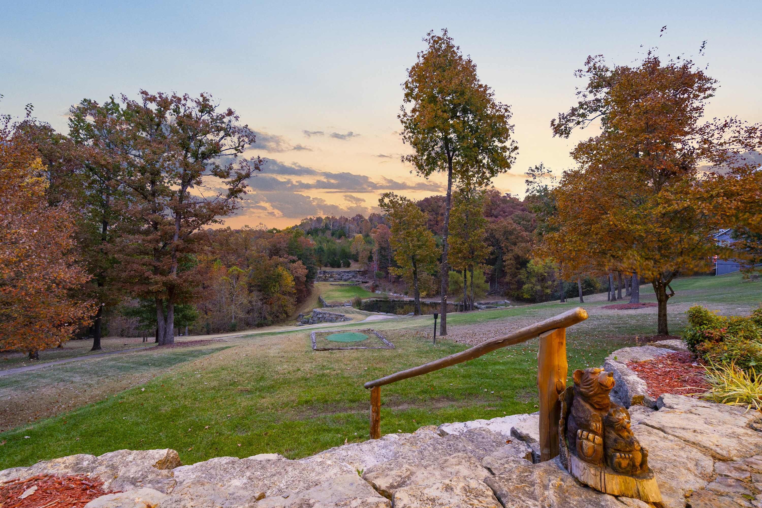 Eine Steinsitzbank mit Holzwertung, die auf einen Park mit herbstlich gefärbten Bäumen und einen entfernten Blick auf einen Golfplatz blickt.