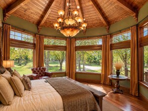 A bedroom with a large bed, a chandelier, multiple windows, and a view of a park.