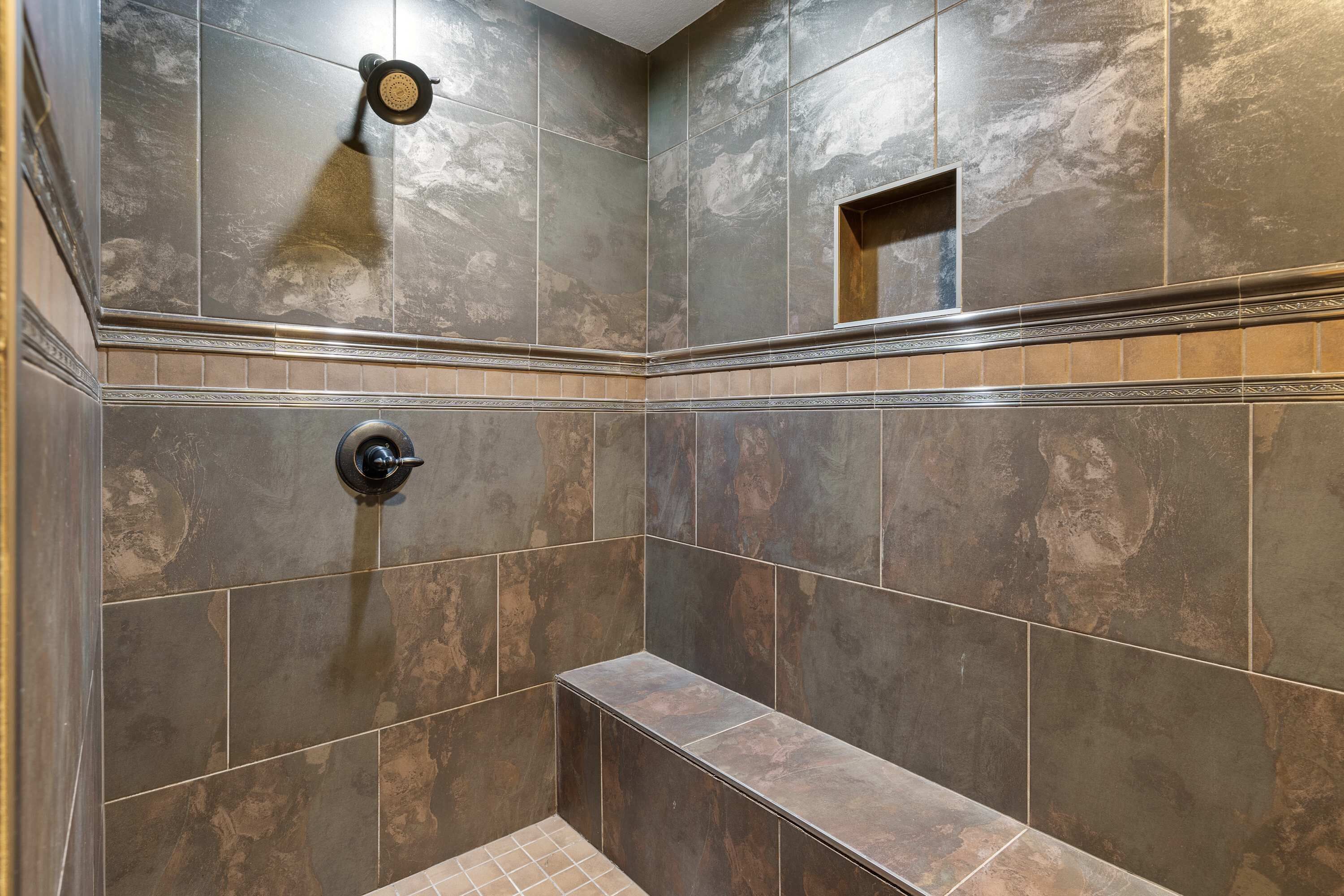 Un espace douche avec des carreaux de pierre foncée, un banc et une pomme de douche.
