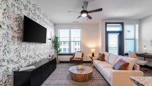 A modern living room with a flat-screen TV mounted on the wall, a ceiling fan, a sofa, a coffee table, and a large window with blinds. - Bennet at Bullstreet (Columbia)