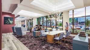 Un moderno vestíbulo de hotel con un amplio comedor, asientos cómodos y grandes ventanales que ofrecen vistas al exterior.