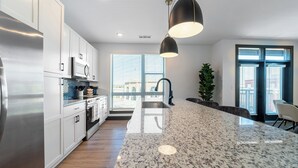 A modern kitchen with white cabinets, a stainless steel refrigerator, a granite countertop, and pendant lighting. - Bennet at Bullstreet (Columbia)