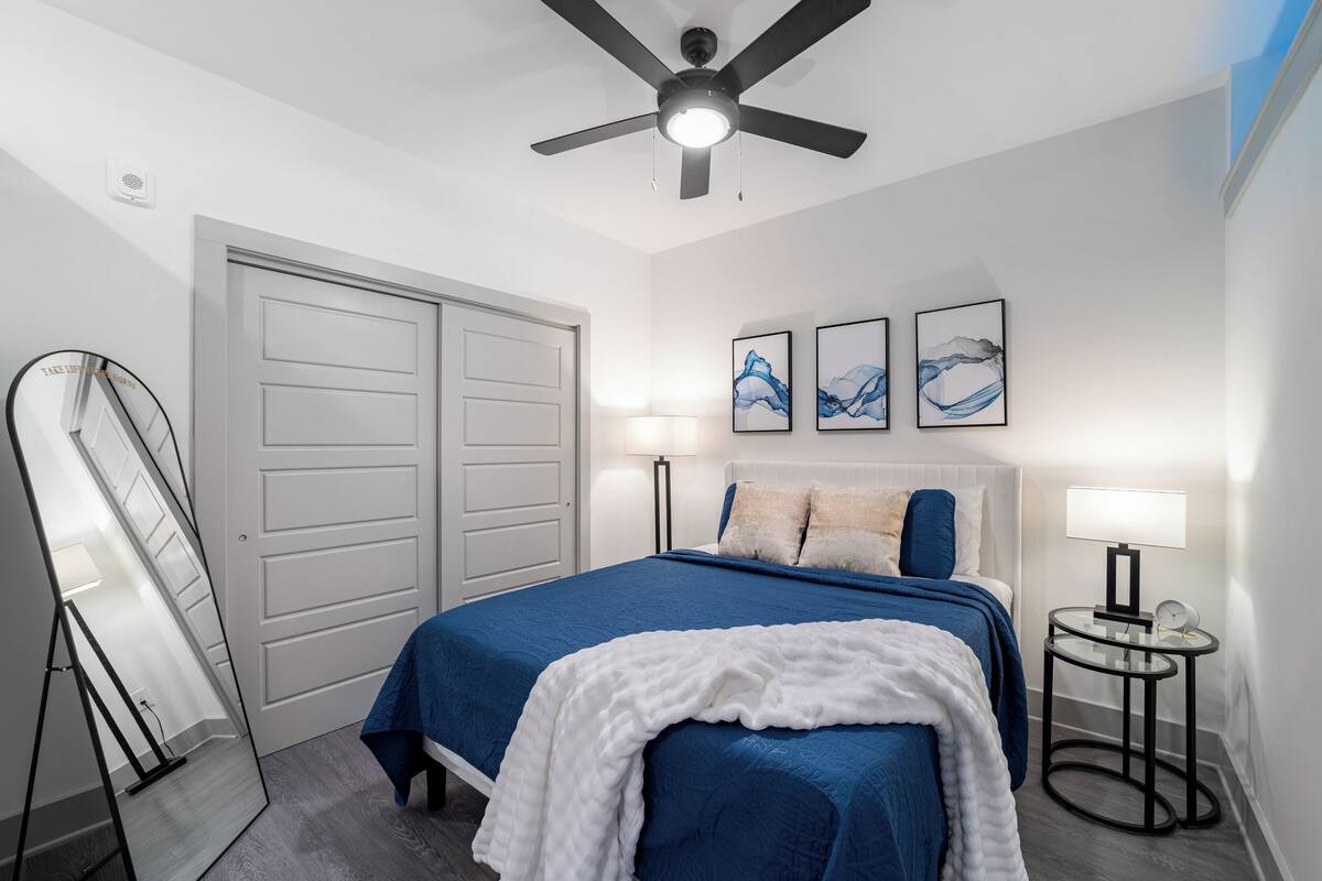 A bedroom with a bed, bedside lamps, a ceiling fan, and artwork on the wall.