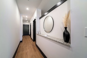 Un pasillo con suelo de madera, un mostrador de recepción con un espejo, un jarrón y una puerta al final.