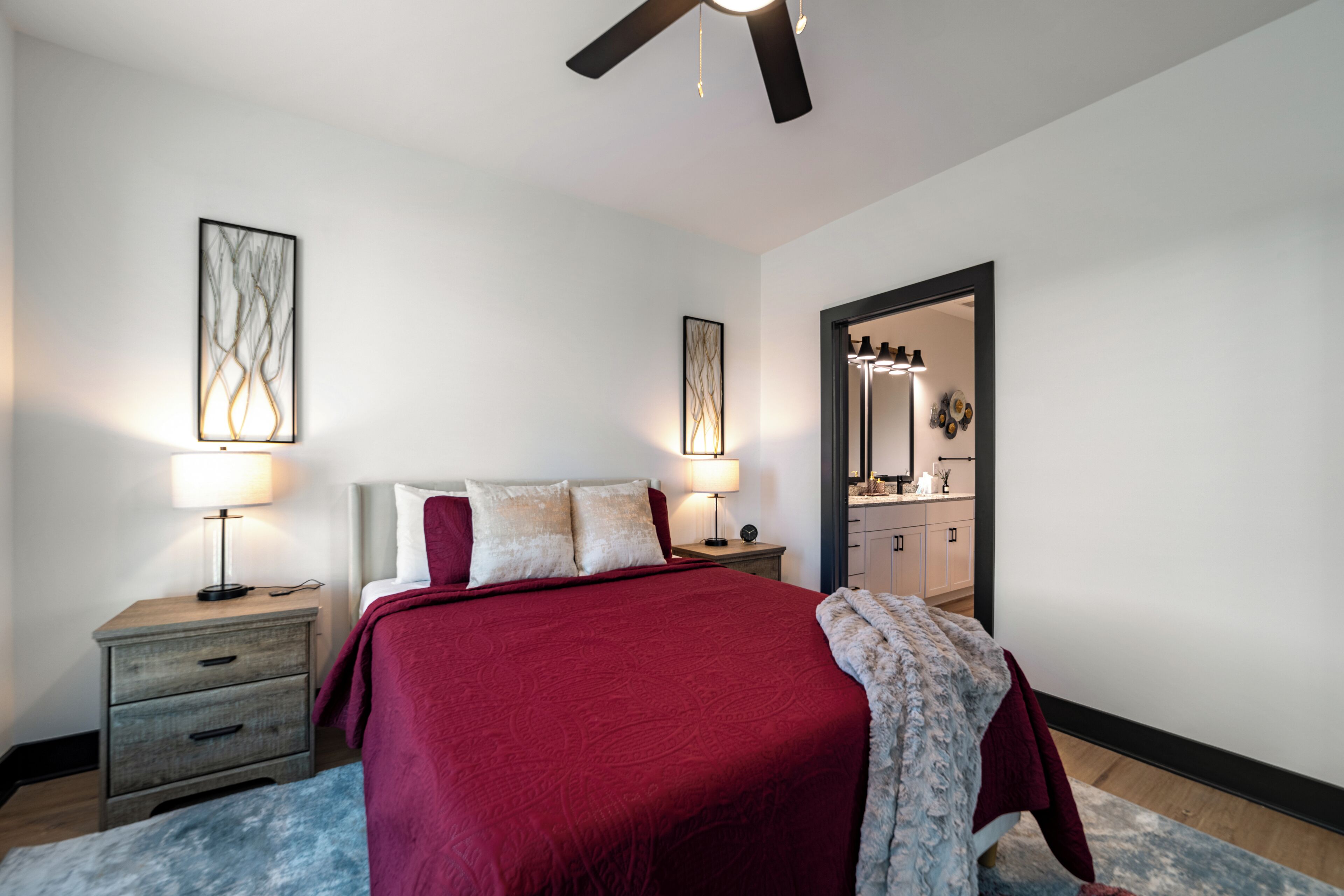 A bedroom with a large bed, two bedside tables with lamps, a ceiling fan, and a mirror in the doorway.