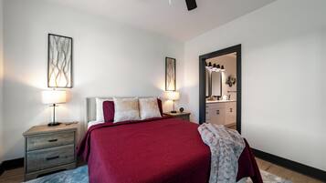 A bedroom with a large bed, two bedside tables with lamps, a ceiling fan, and a mirror in the doorway.