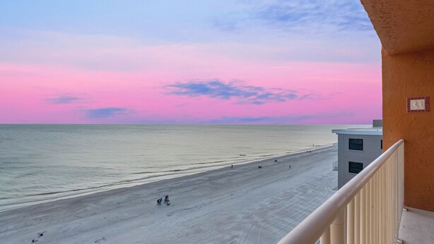 A beach view from a balcony with a clear sky and calm sea.