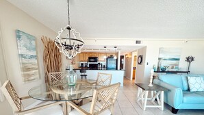 A modern kitchen with a central island, wooden chairs, and a glass dining table.