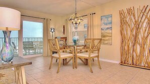 A dining area with a round table, four chairs, a chandelier, and a view of the outdoors.