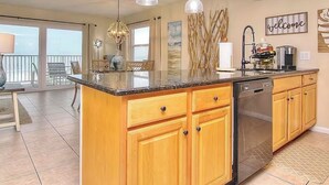 A kitchen with wooden cabinets, a dishwasher, and a countertop. There is a dining area with a table and chairs visible through a glass door.