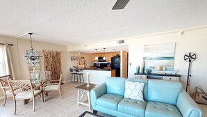 A spacious living room with a blue sofa, a glass coffee table, and a dining area with chairs and a chandelier.