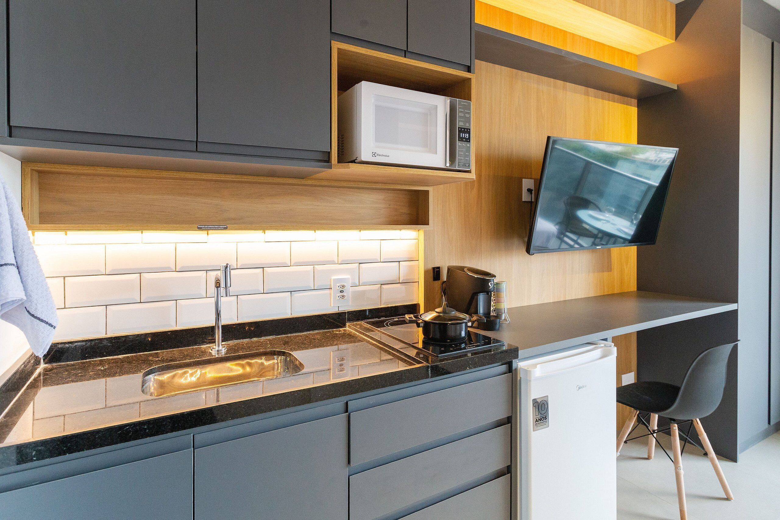 Una cocina moderna con microondas integrado, un lavamanos y un refrigerador pequeño.