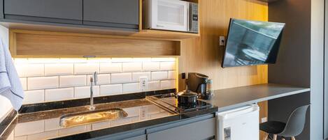 Una cocina moderna con microondas integrado, un lavamanos y un refrigerador pequeño.
