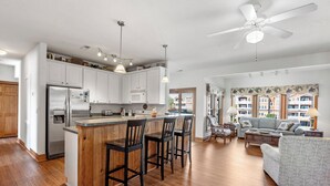 Cocina moderna con isla central, taburetes de bar y zona de comedor con sofá y mesa de centro.