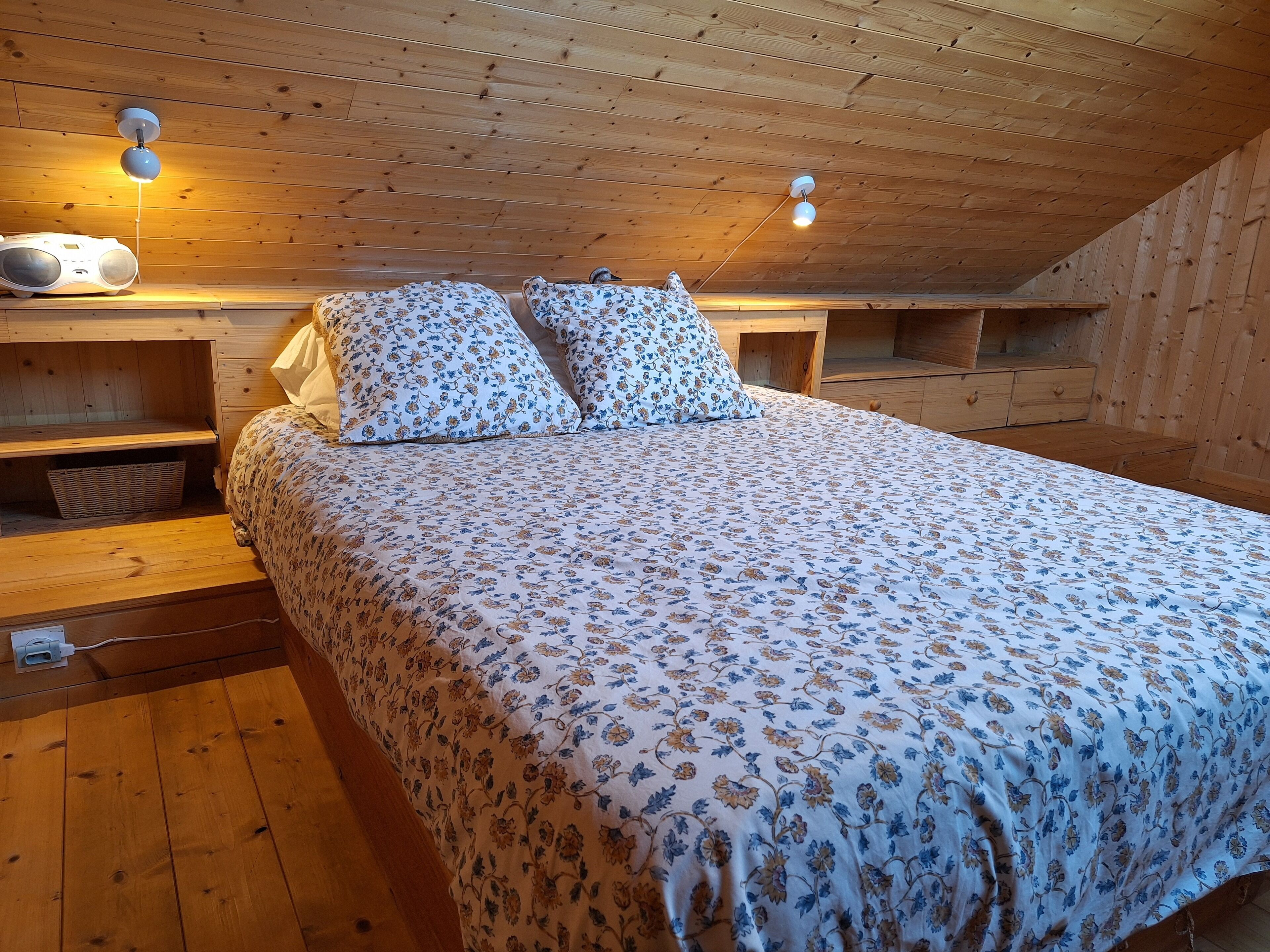 Un dormitorio de cabaña de madera con cama, dos mesitas de noche, una lámpara y una estantería en la pared.