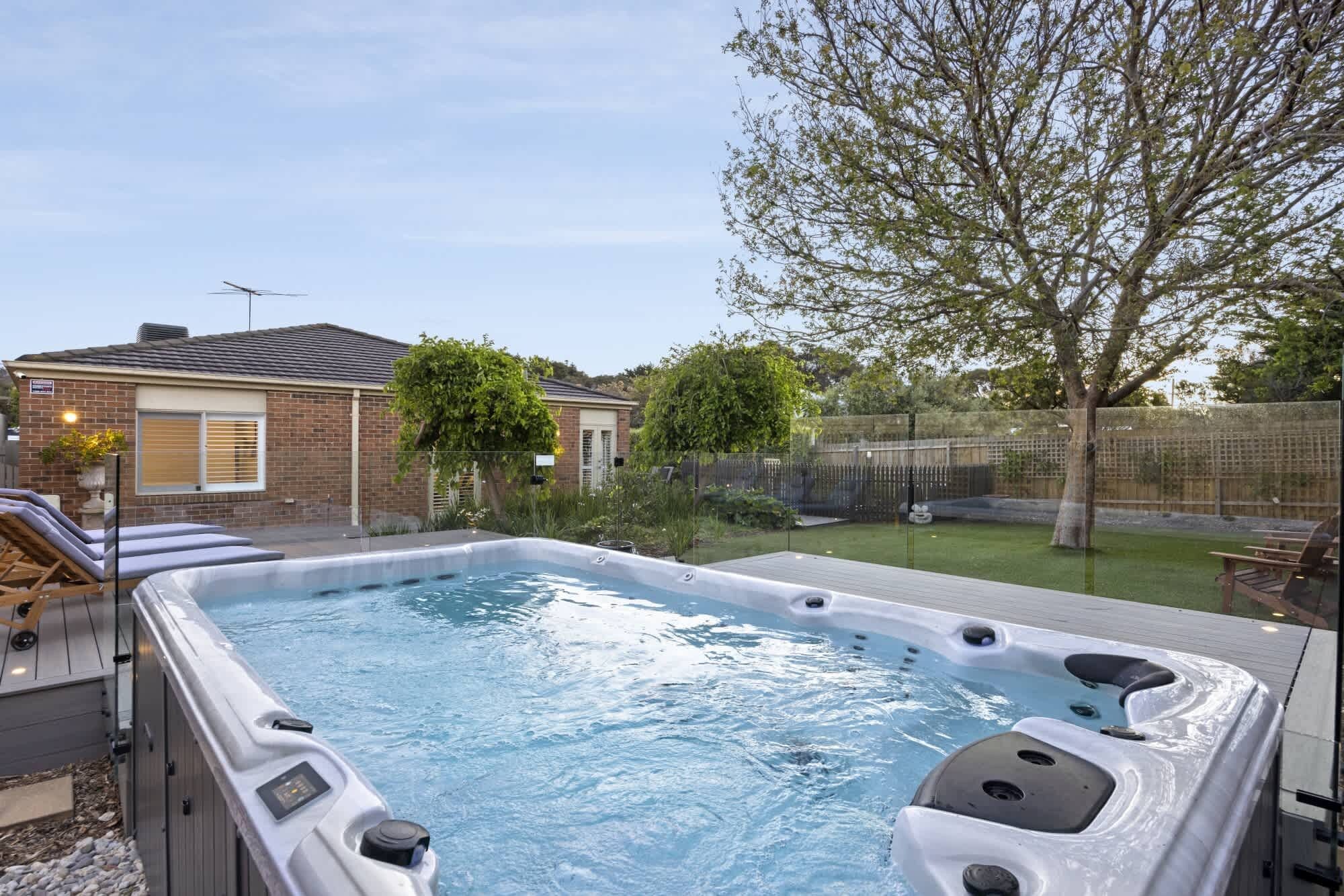 A hot tub in a backyard with a brick house, a tree, and a fence.