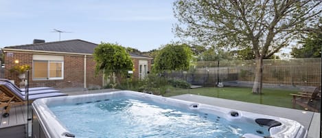 A hot tub in a backyard with a brick house, a tree, and a fence.