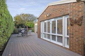 A deck with a table and chairs, a brick wall, and a window with blinds.