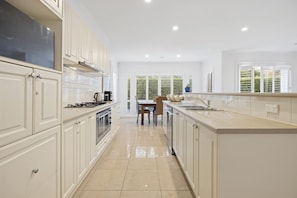 A modern kitchen with white cabinetry, a central island, and a dining area with a view of greenery.