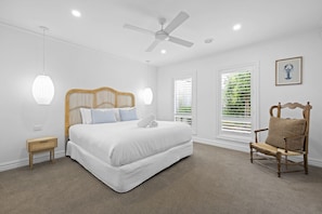 A bedroom with a bed, a chair, a ceiling fan, and two windows with blinds.