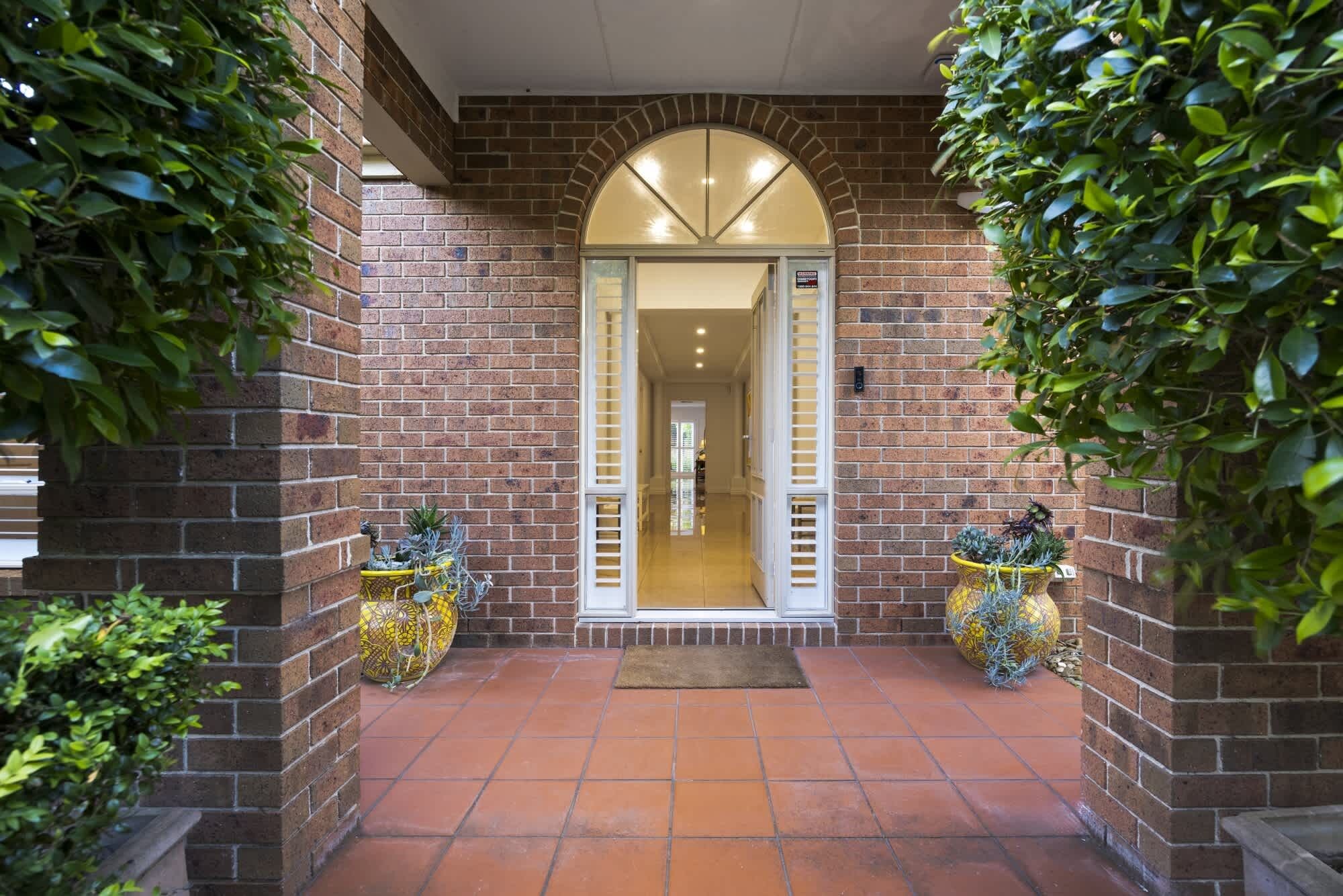 A brick entrance with a tiled patio leading to a well-lit interior.