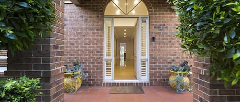 A brick entrance with a tiled patio leading to a well-lit interior.