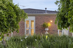 A brick house with a tiled roof, a chimney, and a garden with tall grasses and a potted plant.