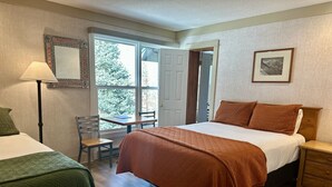 A hotel room with a bed, a desk, a chair, a nightstand, and a lamp.