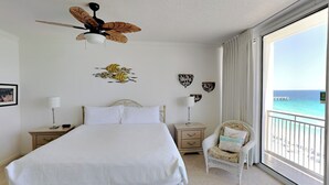 Een slaapkamer met een groot bed, een plafondventilator, een stoel en uitzicht op de oceaan.