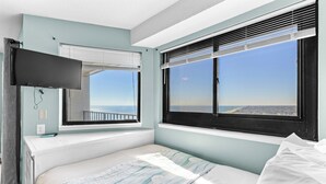 Un dormitorio con cama, televisor montado en la pared y ventanas amplias con vista a la ciudad.
