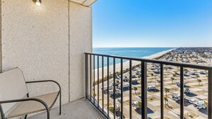 Un balcón con una silla, un muro de concreto y vistas a la playa y un estacionamiento.