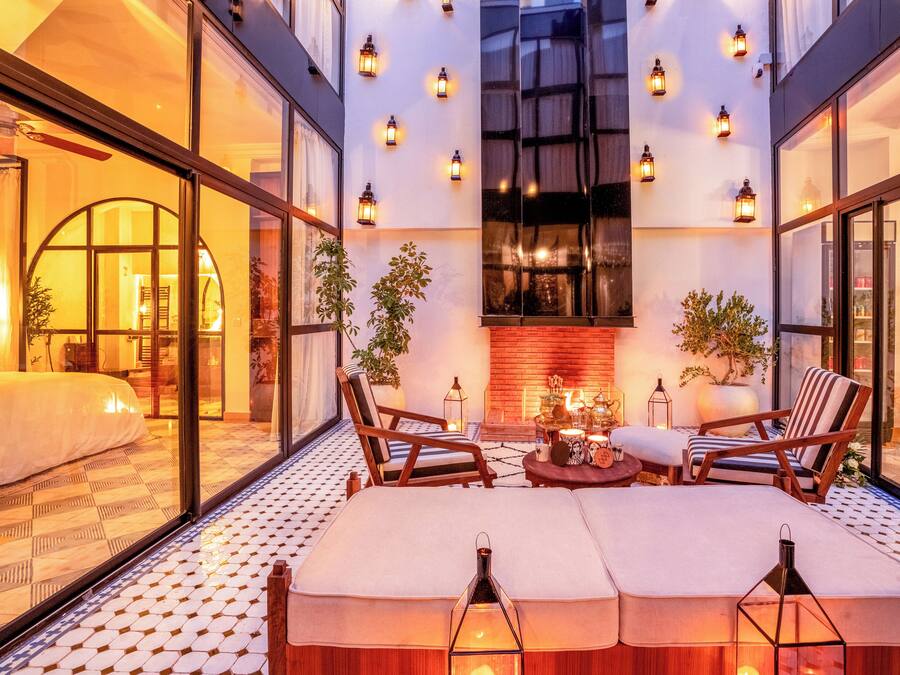 Una habitación de hotel moderna con una cama grande, dos sillones, una mesita con velas y una chimenea.