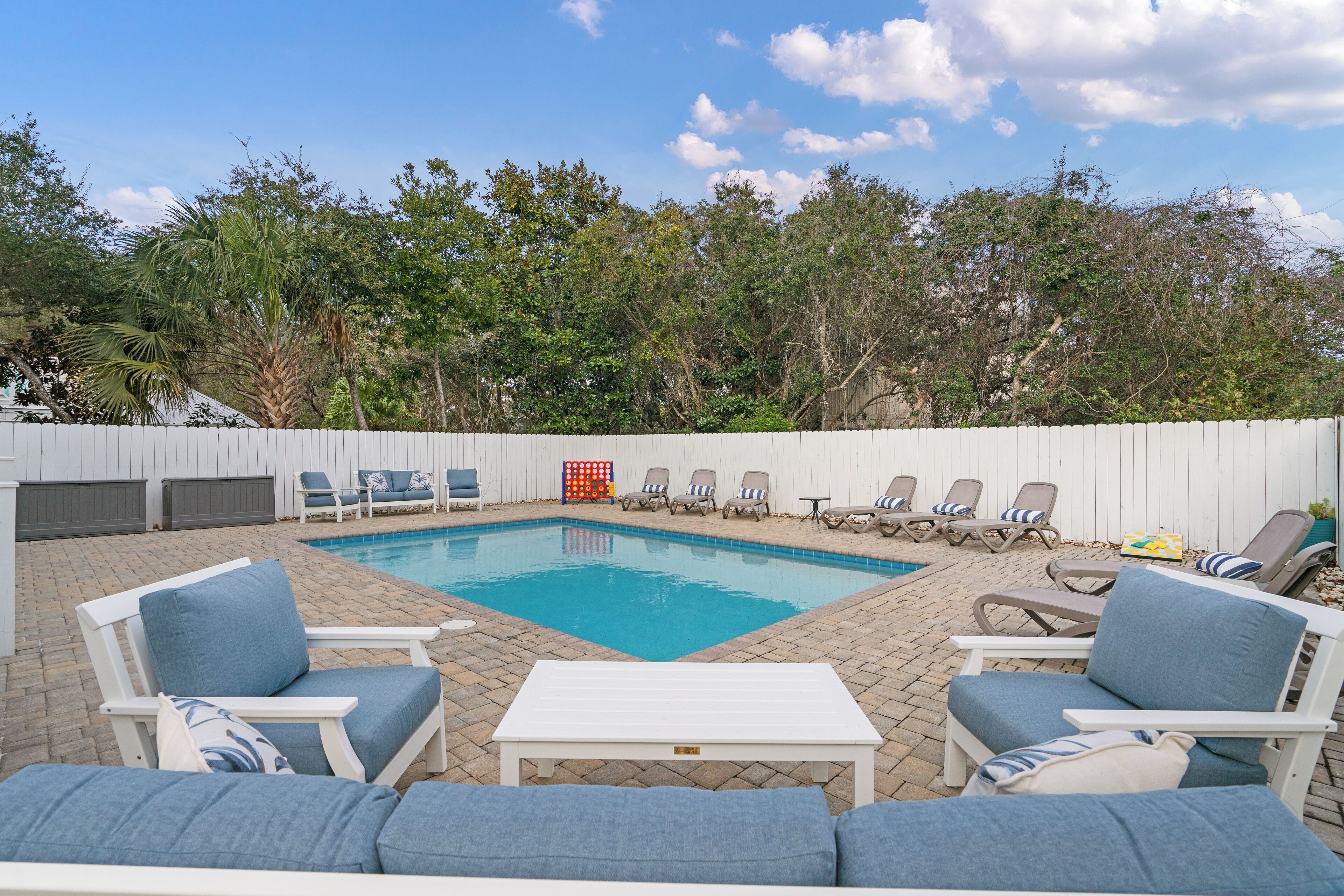 Un patio trasero con piscina, sillas de descanso y una valla blanca.