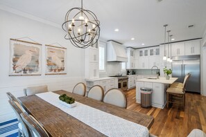 A modern kitchen with white cabinets, a stainless steel refrigerator, and a wooden dining table with chairs. - Coconut Cove-Private Pool, Golf Cart, Bikes, Walk to Beach, Discount Rates. (Santa Rosa Beach)