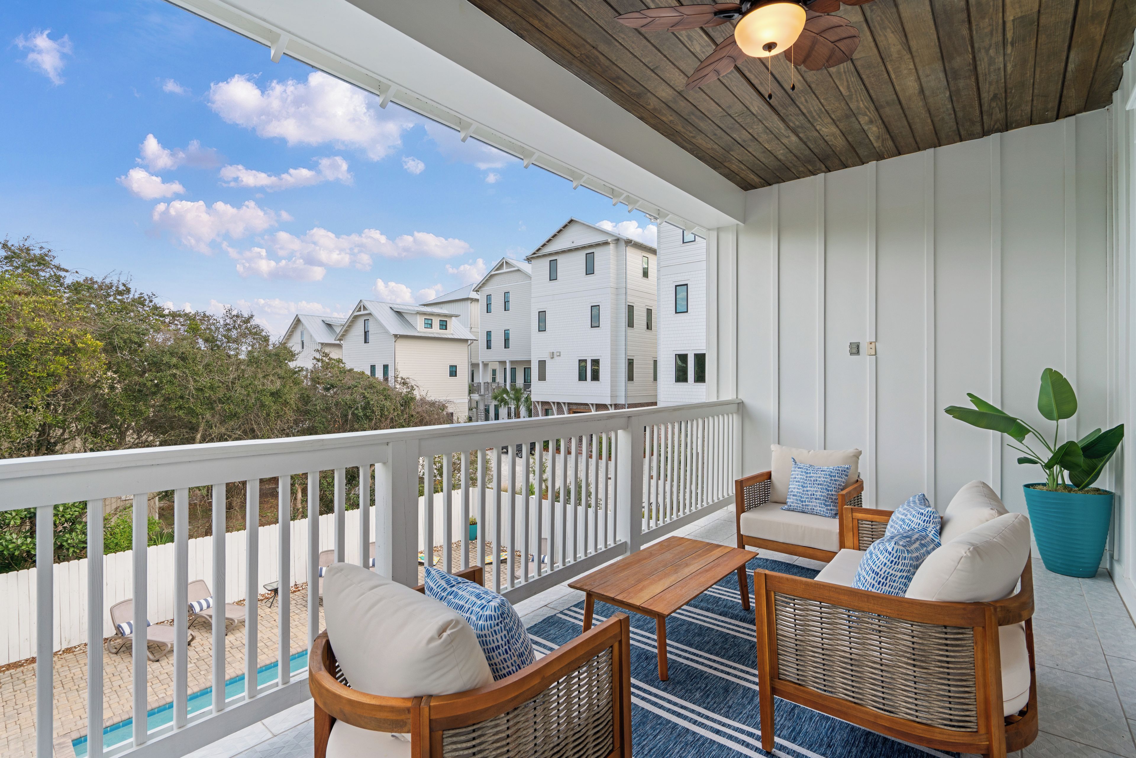 A covered balcony with wicker furniture, a potted plant, and a view of neighboring houses.