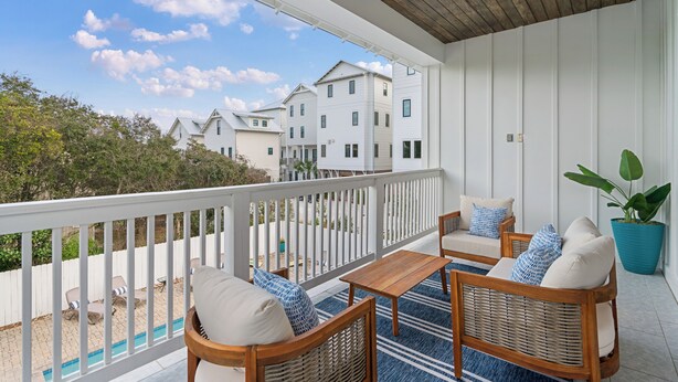 Ein überdachter Balkon mit Korbmöbeln, einem Blumentopf und Blick auf Nachbarhäuser.