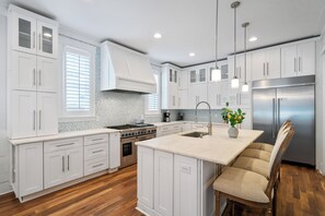 A modern kitchen with white cabinetry, a central island, a stainless steel refrigerator, and a wooden chair. - Coconut Cove-Private Pool, Golf Cart, Bikes, Walk to Beach, Discount Rates. (Santa Rosa Beach)