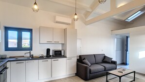 A modern kitchen with white cabinets, a microwave, and a coffee maker. There is a gray sofa and a small table with a rug. - Charming sheepfold on the Liamone beach (Casaglione)