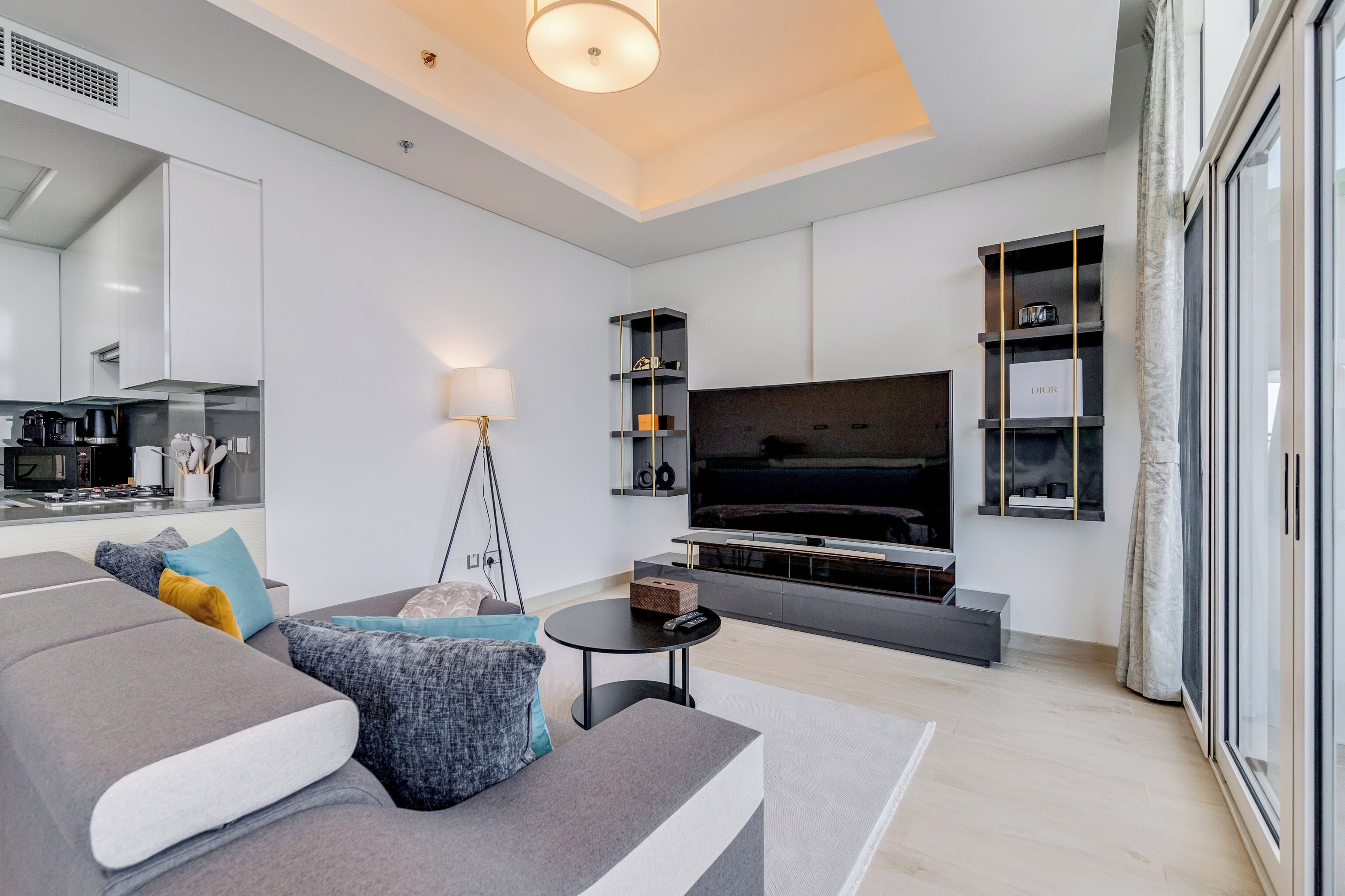A modern living room with a grey sofa, a flat-screen TV, and a minimalist kitchen in the background.