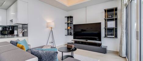 A modern living room with a grey sofa, a flat-screen TV, and a minimalist kitchen in the background.