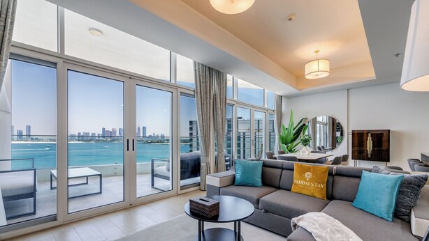 A modern living room with a large window overlooking a city skyline and water. - Globalstay Luxury Azizi Mina Beachfront  (Dubai)