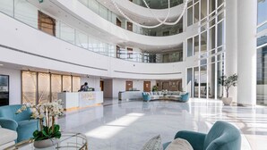 A spacious lobby with a central seating area, a reception desk, and a modern architectural design with glass railings and a high ceiling. - Globalstay Luxury Azizi Mina Beachfront  (Dubai)