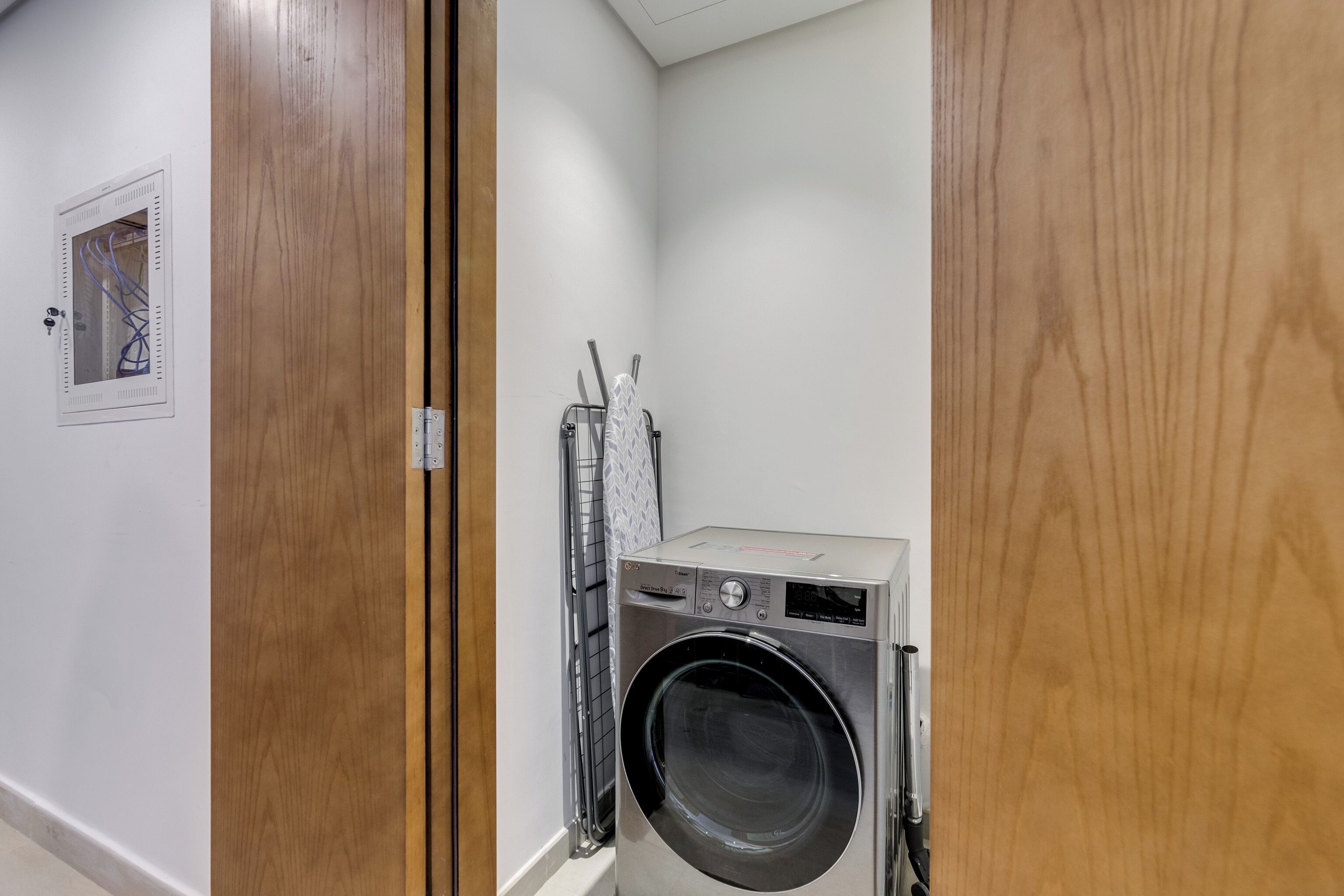 A compact laundry room with a front-loading washing machine, a metal rack, and a door with a wooden frame.