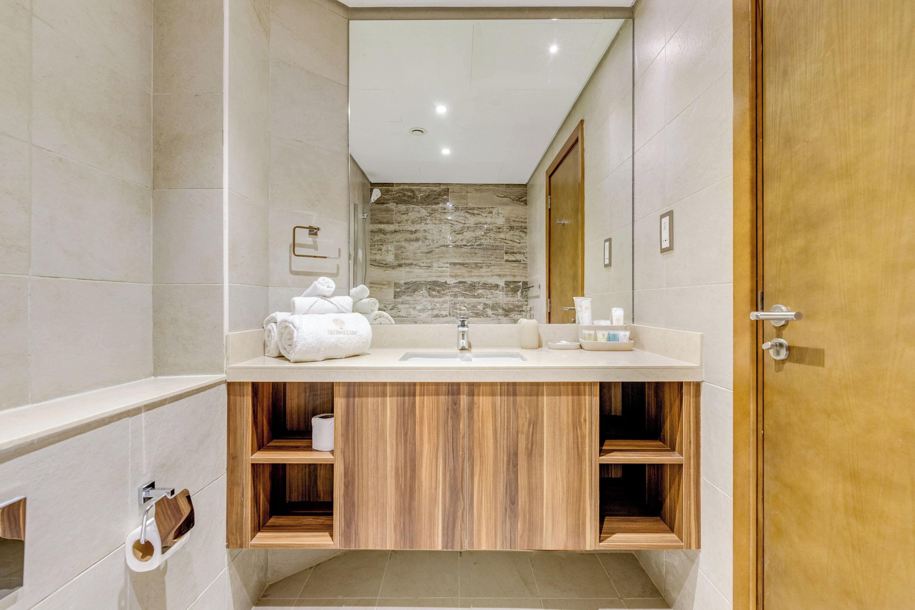 A modern bathroom with a large mirror, a sink, and wooden cabinetry.
