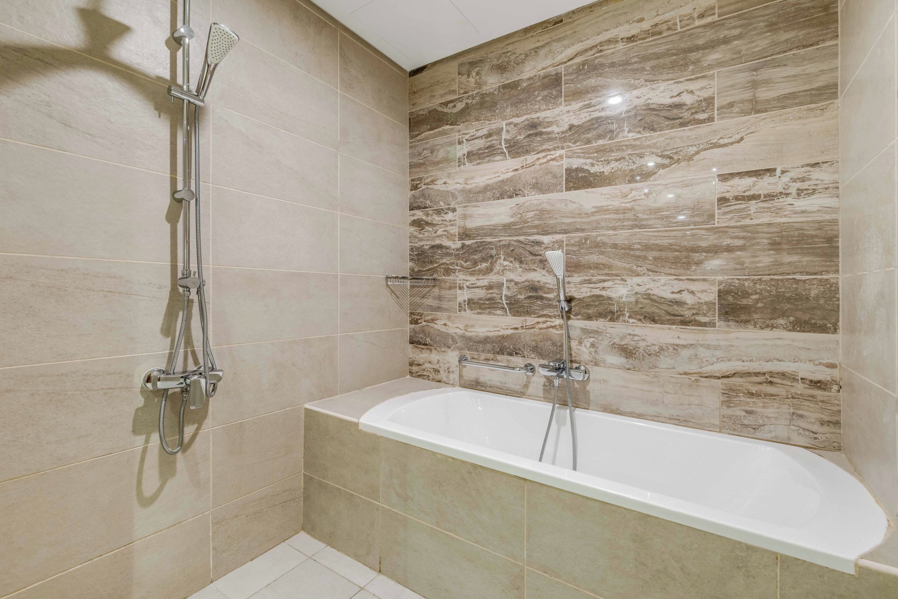 A bathroom with a bathtub, a shower, and a wall with a marble-like tile pattern.