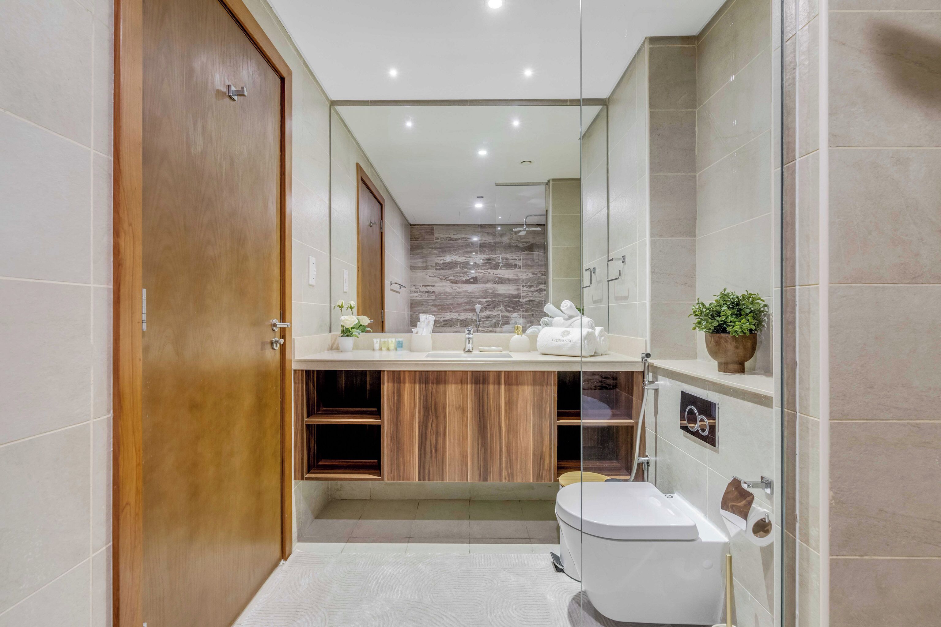 A modern bathroom with a wooden door, a vanity with a marble backsplash, a toilet, and a shower area.