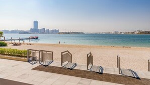 A beach with a view of a city skyline, including a tall tower, and a promenade with metal railings and chairs. - Globalstay Luxury Azizi Mina Beachfront  (Dubai)