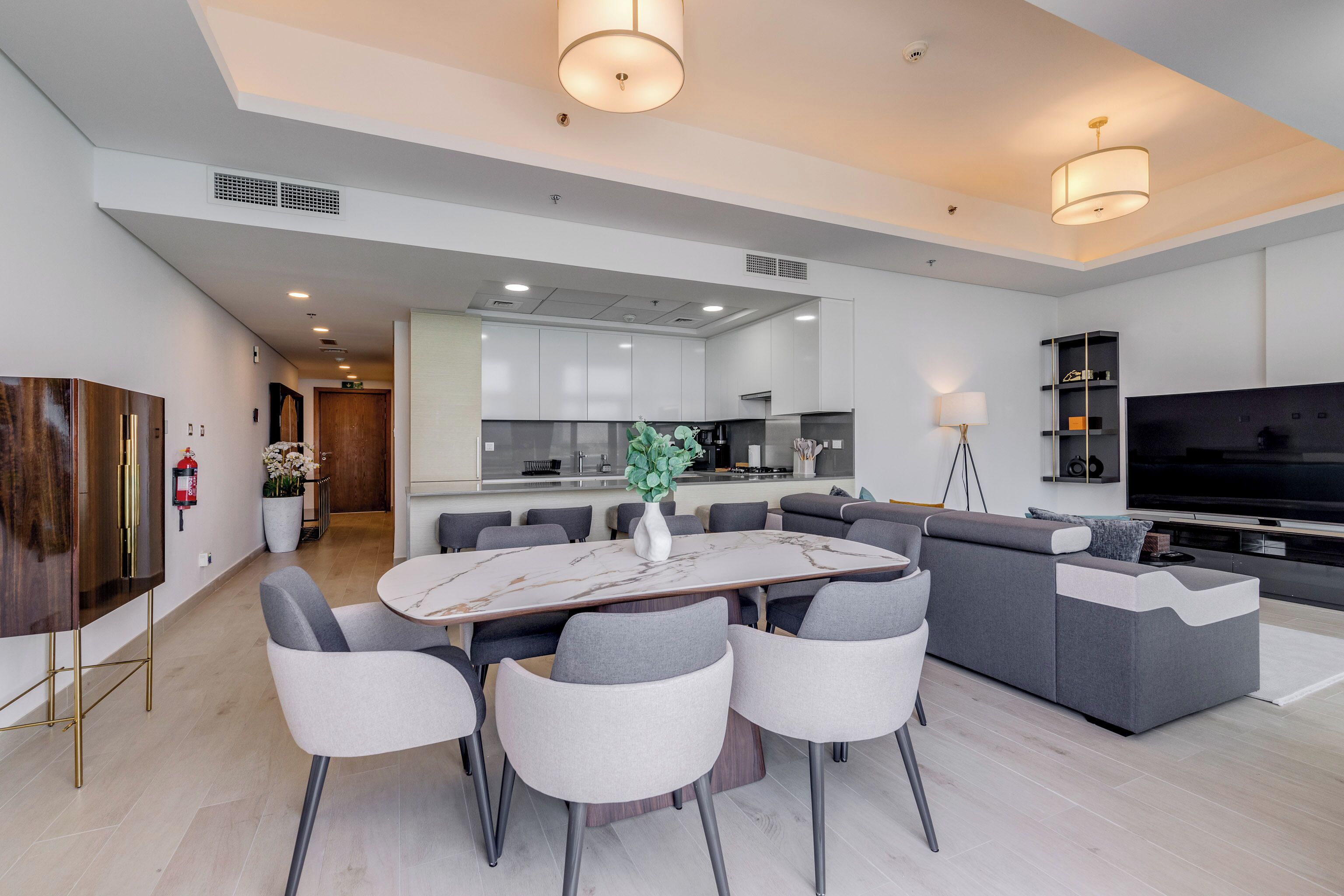 Una sala de estar moderna con comedor, un sofá, un televisor y una cocina al fondo.